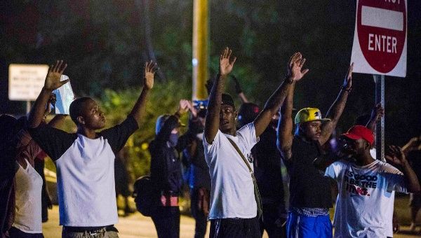 Demonstrators stand in the middle of West Florissant holding a street sign, with their hands up, towards the police. (Photo:Reuters)