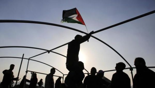 A Palestinian hangs a Palestinian flag as others erect the steel frames of a tent at a land that they said was confiscated by Israel, during a protest against land confiscations near the West Bank town of Abu Dis near Jerusalem February 3, 2015.