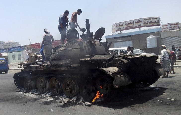 People stand on a tank that was burnt during clashes on a street in Yemen's southern port city of Aden March 29, 2015.