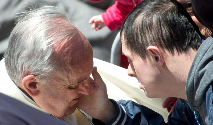 El papa Francisco recibe la caricia de un joven con síndrome de Down.