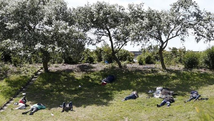 Varios personas descansan en un terreno situado cerca de la entrada del Eurotúnel, cerca de Calais.