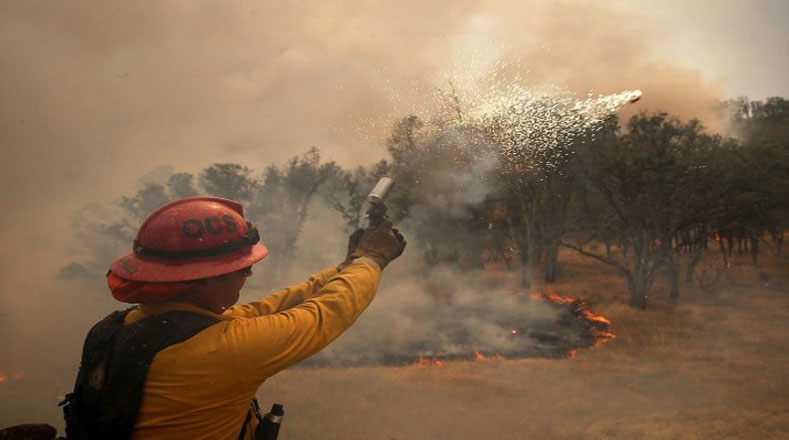 Un bombero se aleja de una llama alta mientras intentaba quemar la hierba para evitar que el fuego se propague.
