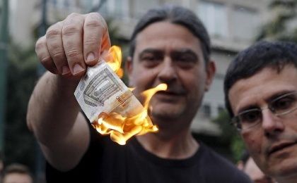 Manifestantes anti-austeridad queman un billete del euro durante una manifestación frente a las oficinas de la Unión Europea (UE) en Atenas, Grecia 28 de junio de 2015. 