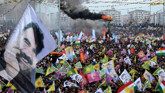 Humo se eleva desde un fuego encendido mientras la gente ondea banderas kurdas y fotos de su líder encarcelado,AbdullahOcalan y celebranNewroz, el Año Nuevo kurdo, en la ciudad turca de Diyarbakir, el 21 de marzo de 2015.