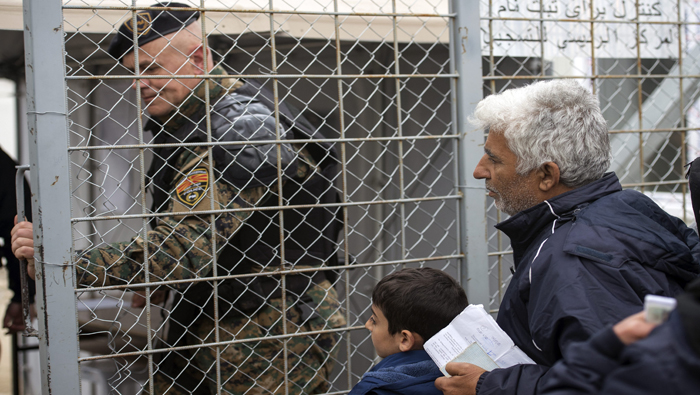 Un policía macedonio cierra el acceso fronterizo delante de un grupo de refugiados que esperan entrar en Macedonia desde Grecia.