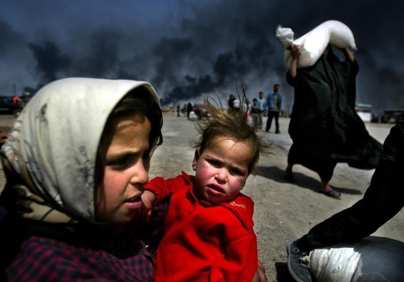 An Iraqi girl holds her sister as she waits for her mother (R) to bring over food bought in Basra March 29, 2003. 