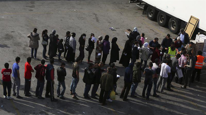 Varias personas hacen cola para recibir alimentos en el campamento para refugiados ubicado en el puerto del Pireo en Grecia.