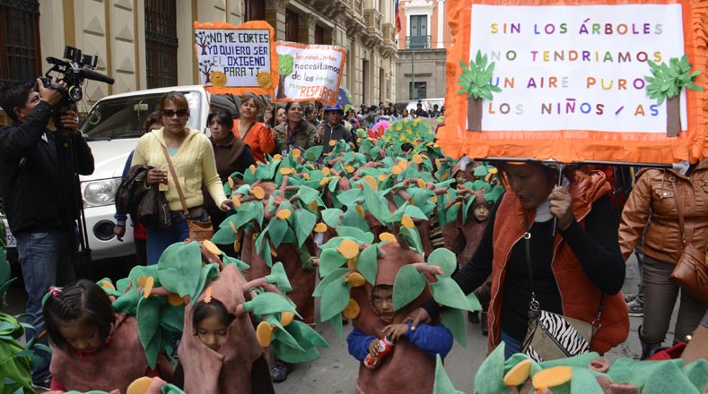 Niños disfrazados de árboles y portando pancartas para llamar la atención sobre el cuidado de la Tierra.