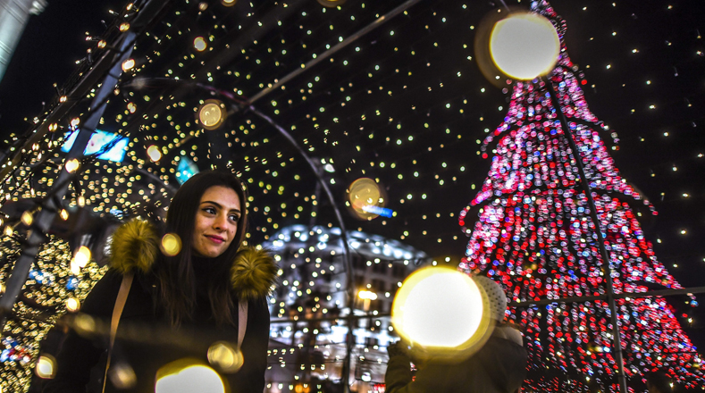 La plaza central de Skopie en Macedonia es alumbrada por un árbol navideño. Una mujer pasea debajo de un túnel iluminado. 
