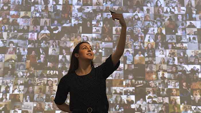 Una mujer posa para un selfi ante una pantalla con miles de imágenes de personas en las redes sociales.