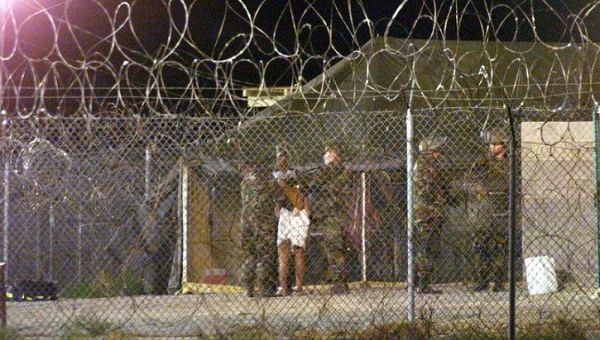 Marines at Camp X-Ray at the Naval Base at Guantanamo Bay, Cuba escort a newly arriving detainee into a processing tent.