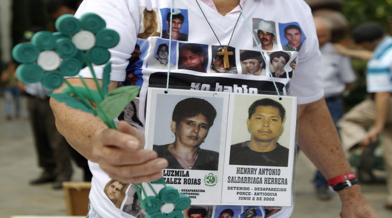 Una persona muestra fotografías de sus familiares desaparecidos mientras participa en un plantón realizado en Colombia, en conmemoración del Día Internacional de la Desaparecido Forzada.