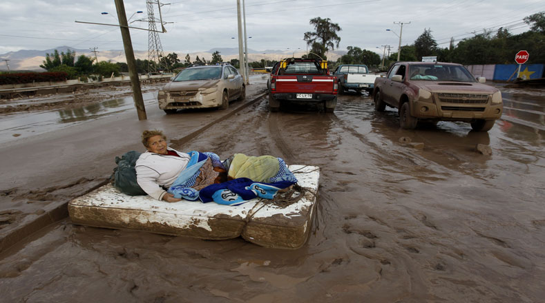 Una mujer descansa sobre un colchón en una calle cubierta de barro, tras inundación en Copiapó, capital de la región de Atacama.