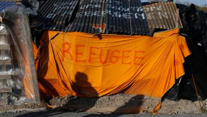 Las sombras de los migrantes se reflejan en un refugio improvisado con la palabra  ' refugiados' en Calais, Francia, 30 de abril de 2015.