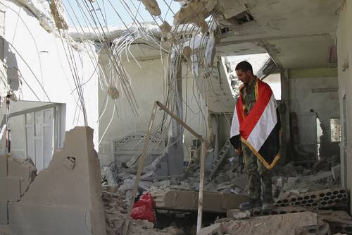Cubierto con la bandera de su país, un soldado sirio observa las ruinas de una casa en Achan, provincia de Hama. Rusia intensificó el lunes pasado ataques contra terroristas del Estado Islámico.