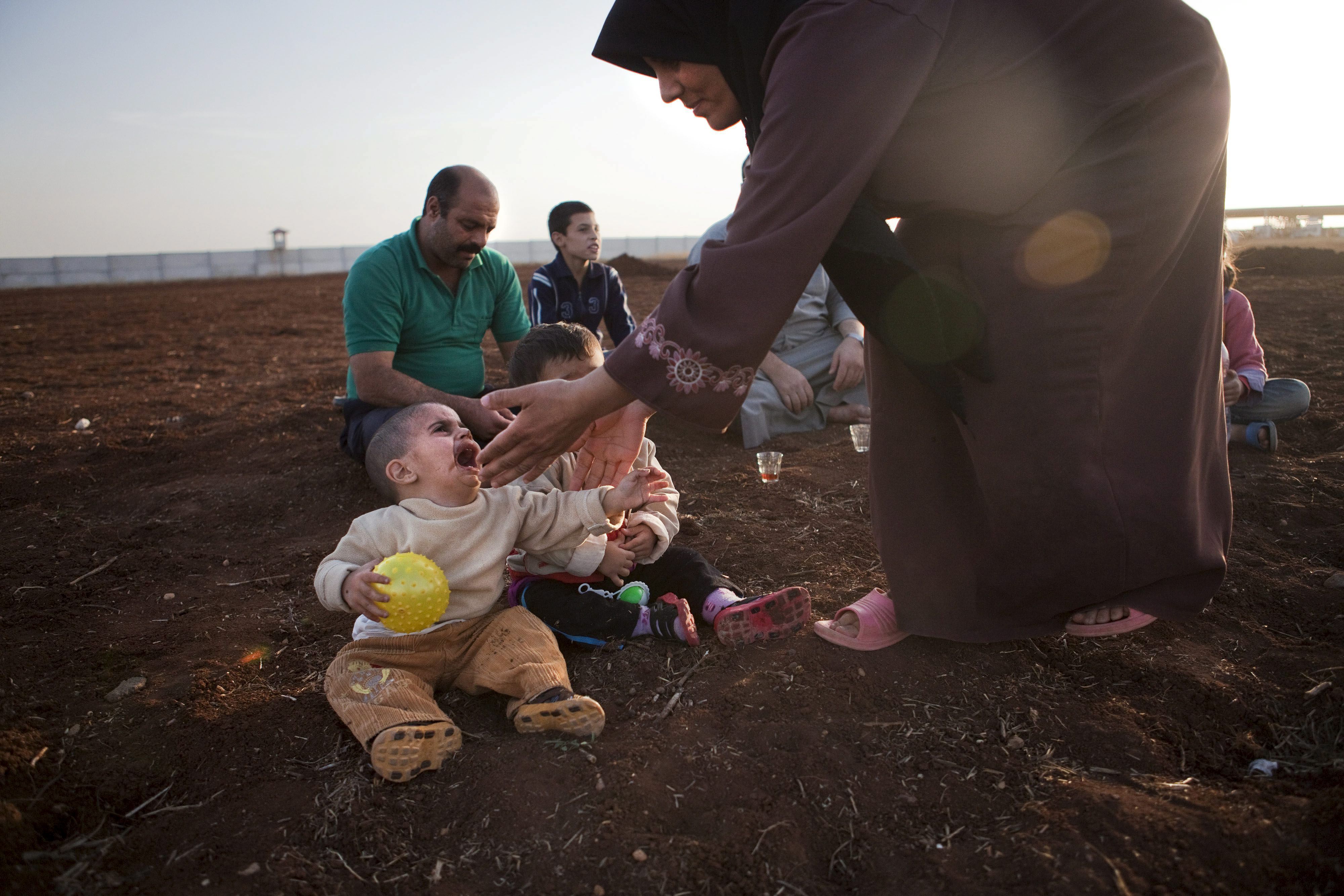 Una refugiada siria tiende su mano hacia unos niños en un campamento de personas desplazadas en la frontera turco-siria cerca de Azaz, Siria.