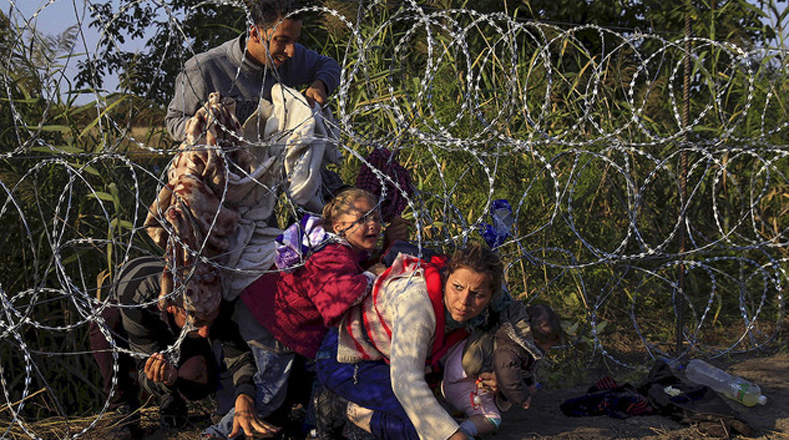 Refugiados sirios cruzan una cerca para entrar a Hungría en la frontera con Serbia.