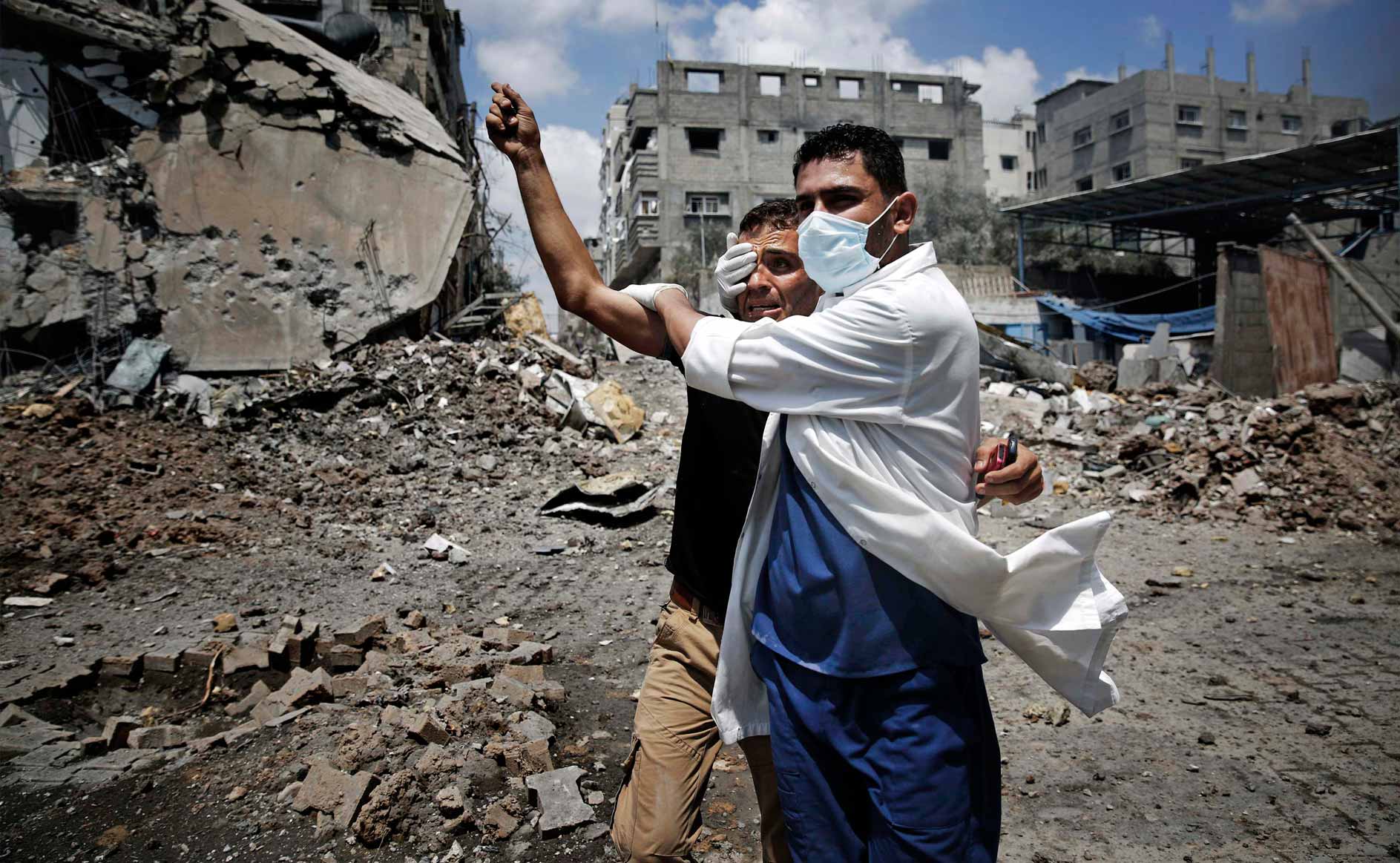 Un sanitario atiende a un palestino entre las ruinas provocadas en Gaza por un bombardeo.