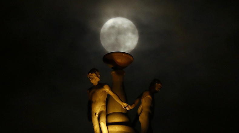 La luna está parcialmente cubierta por las nubes, ya que se eleva detrás de una estatua en la parte superior de la antigua ópera en el centro de Frankfurt, Alemania.