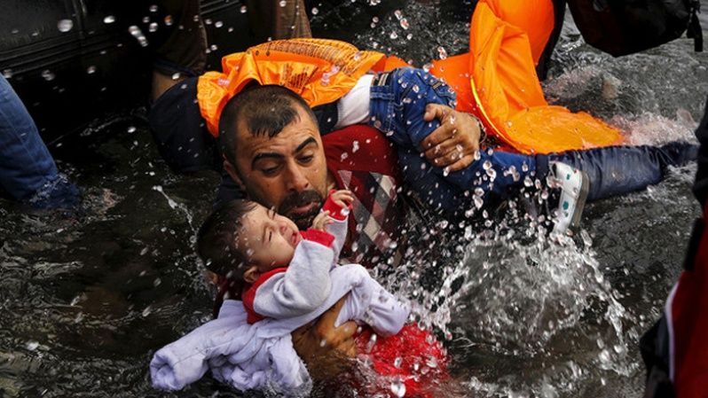 Un refugiado sirio se aferraba a sus hijos mientras luchaba por bajar de un bote en la isla griega de Lesbos.
