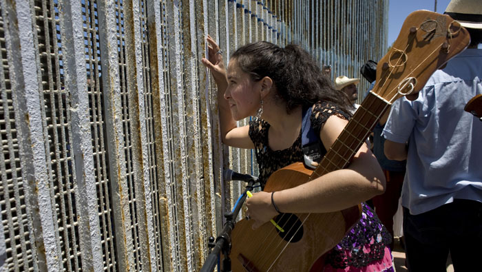 Artista entabla una conversación con otra persona a través del muro entre México y EE.UU. durante el 