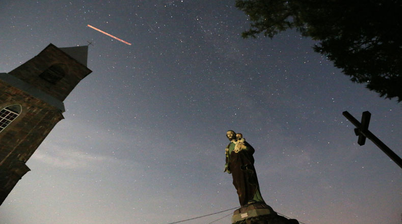 Una estatua católica, una cruz y una iglesia se ven durante la lluvia de meteoritos Perseidas cerca de la aldea de Rubezhevichi, a unos 50 km de Minsk, Bielorrusia.