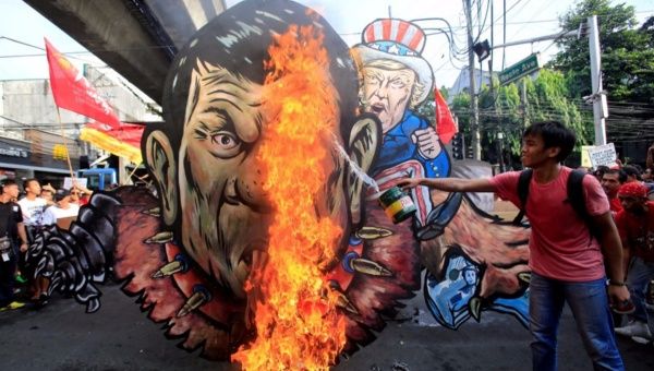 An activist pours gasoline as an effigy of President Rodrigo Duterte and U.S. President Donald Trump burns during a protest action against Duterte