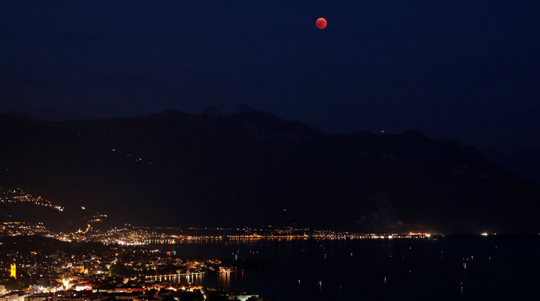 En los Alpes suizos y la montaña Tour de Mayen se observó el eclipse total, la Luna en su máximo punto sobre una ciudad iluminada por las luces de la vida cotidiana.